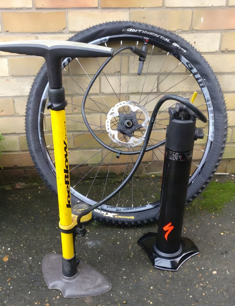 Specialized Air Tool Blast hooked up to a 29er wheel valve beside a yellow Joe Blow track pump against a brick wall.