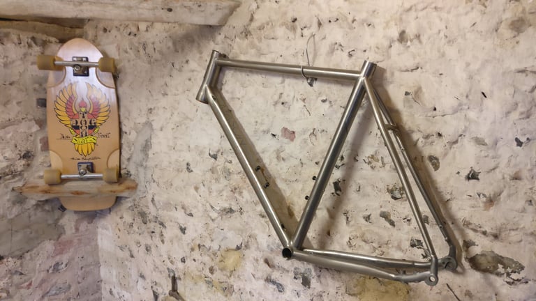 Raw unpainted development frame hung on the flint wall of the Mason Barn, a skateboard with an eagle graphic beside it.