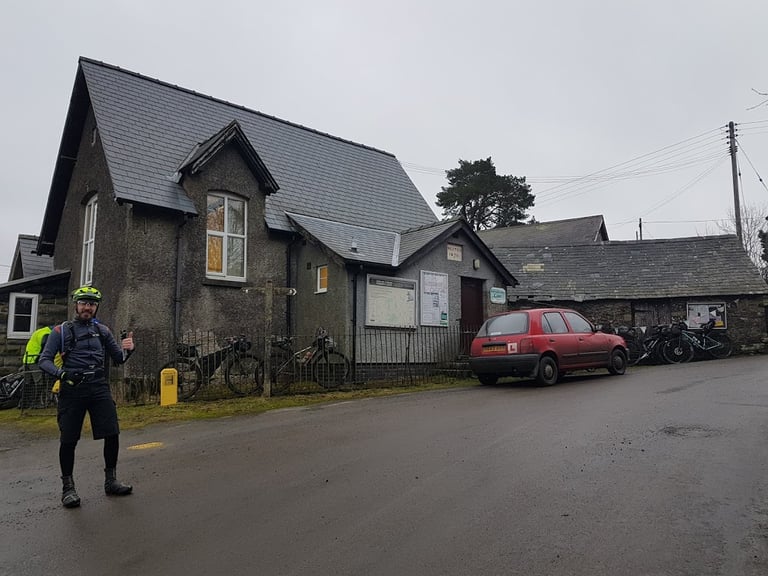 Rider gives a thumbs up outside the Glyndwr Way Café at Bwlch-y-Sarnau, with bikepacking bikes parked along the railings.