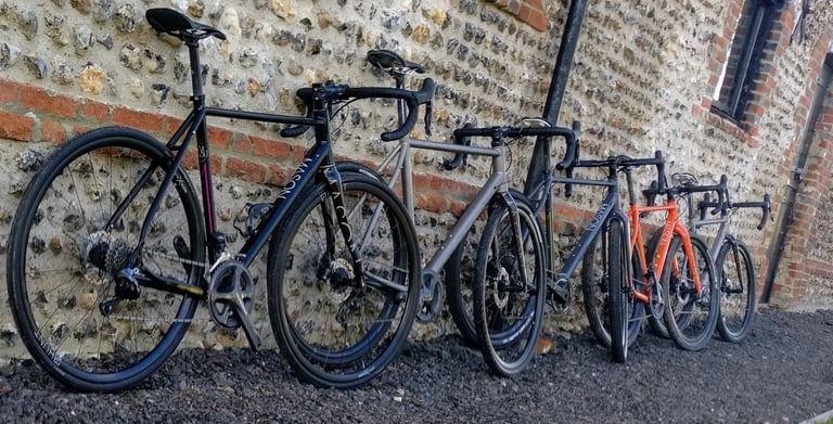 Five Mason road and gravel bikes, one in orange, leaning in a row against a flint and brick wall.