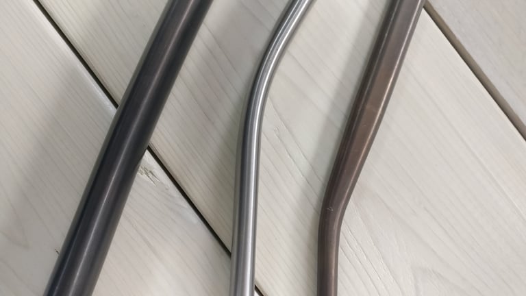 Three bent prototype Mason tubes with custom profiles in dark, polished and bronze finishes on pale wood.