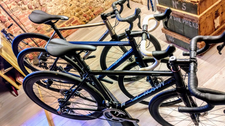 Three Mason bikes seen from above indoors: a black steel Resolution, a blue Definition and a raw titanium Bokeh Ti.