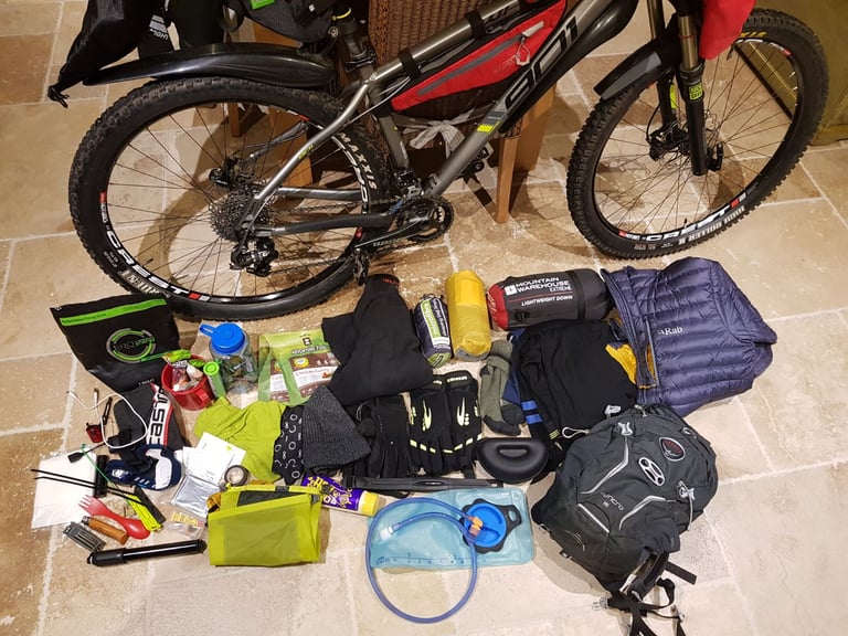 James Pearson's bikepacking kit laid out on the floor beside his bike, including sleeping bag, jacket and gloves.