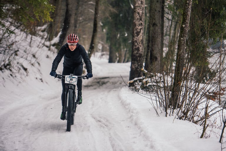 Racer with number 48 rides a 29er mountain bike along a packed snow track through woods at the Snow Bike Festival.