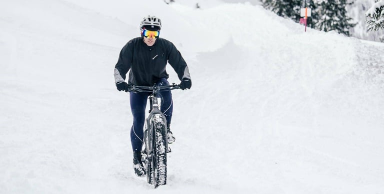Rider in ski goggles grinds a fatbike through deep fresh snow on Stage 1 of the Snow Bike Festival.