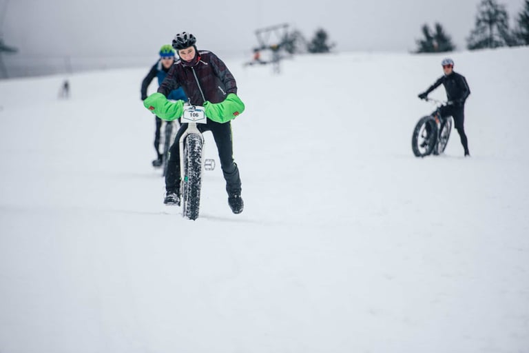 Rider with green handlebar mitts rides a fatbike across a snowy ski slope on Stage 3 of the Snow Bike Festival.