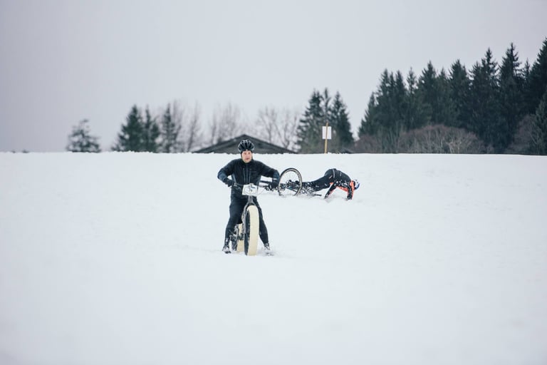 Fatbike rider stands over their bike while another lies in the snow after a fall on the Stage 3 descent.