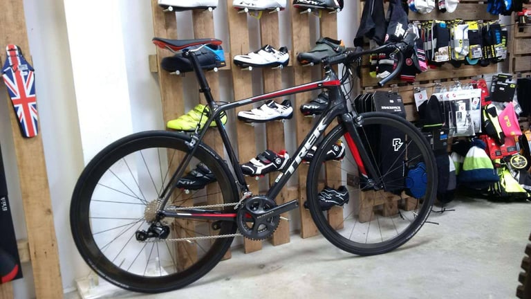 Trek Emonda SL built up with rim brakes and deep carbon wheels, standing in a cycle shop beside racks of shoes.