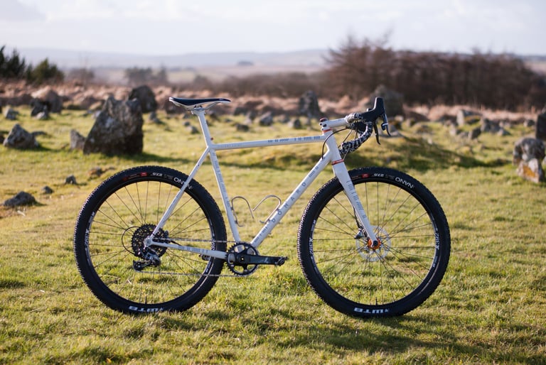 Donard x Victory Chimp steel gravel bike side-on among scattered boulders on open hillside, with hills in the distance.