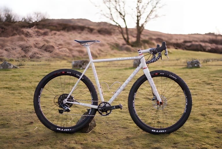Donard x Victory Chimp collaboration gravel bike in white, parked on moorland with standing stones behind.