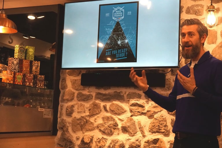 Arnaud Manzanini presents Race Across France at bASECAMP in Talloires, with the race poster on a screen behind him.
