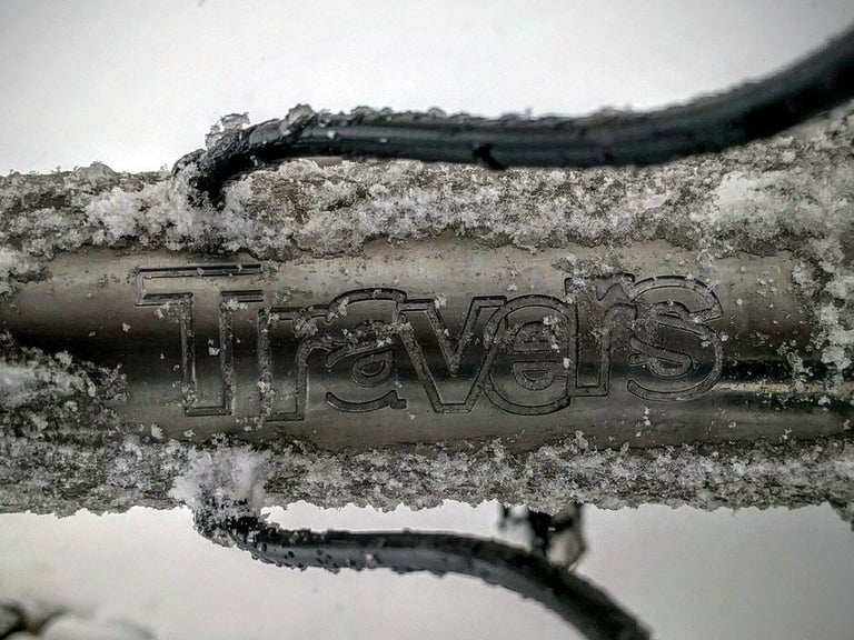 Close-up of the Travers logo on a snow-crusted titanium tube of the Bat Fastard fatbike.