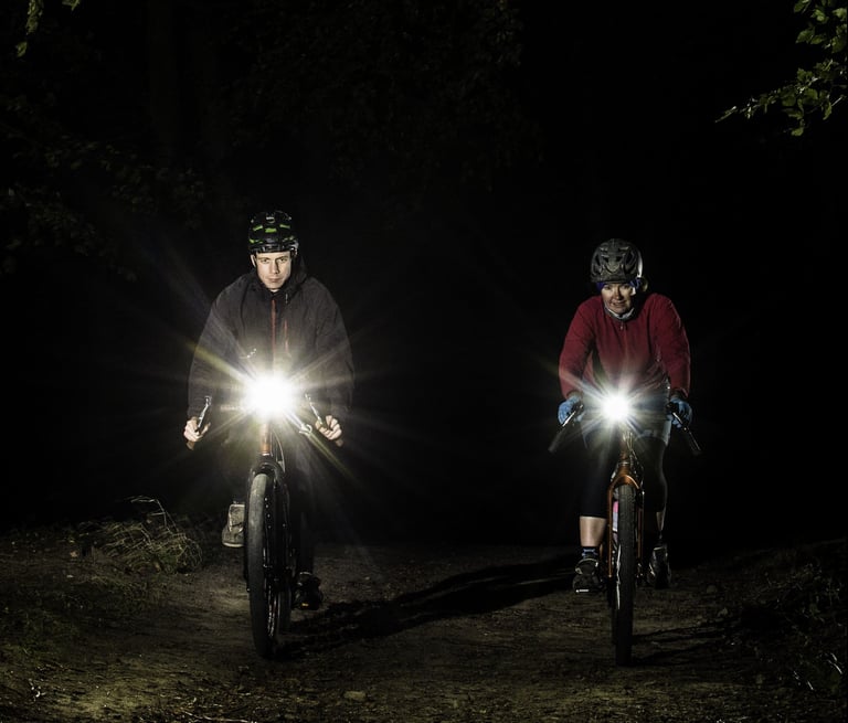 Two riders face the camera on a dark trail, handlebar lights flaring, ahead of the Yorkshire True Grit Dark Skies.