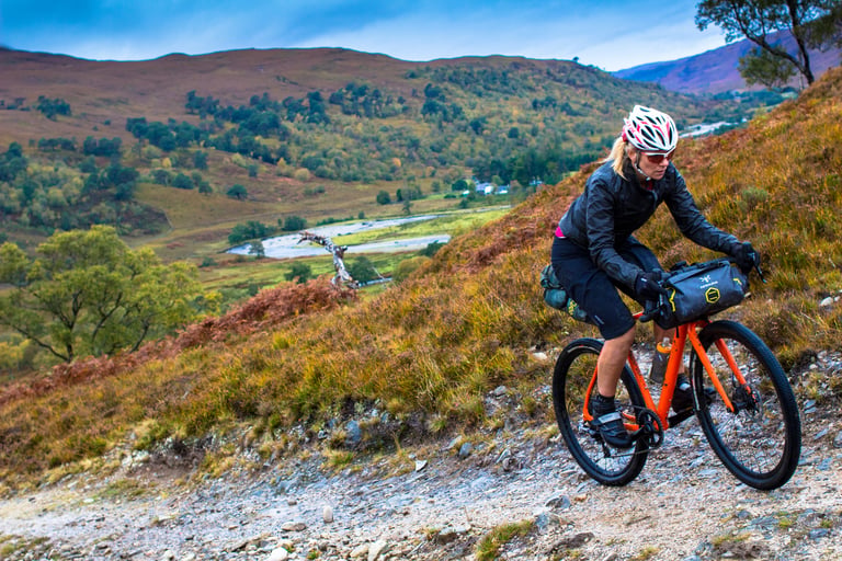 Naomi Freireich climbs a rocky hillside track above a Highland glen on her Mason Bokeh, Apidura bar bag on board.