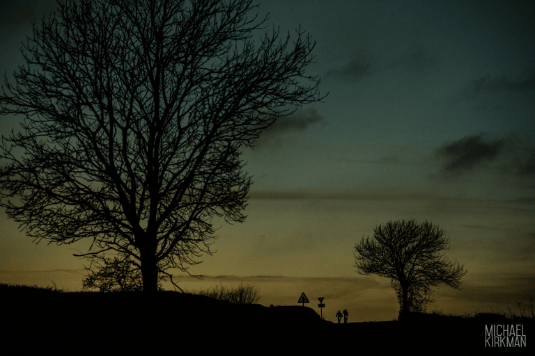 Two distant riders silhouetted at dusk beside bare trees on the North York Moors.