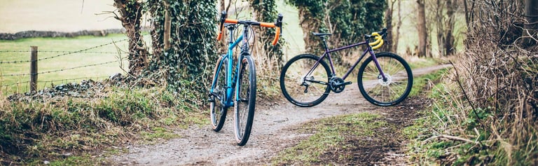 Blue and purple Cotic Escapades side by side on a gravel lane, one front-on and one in profile.