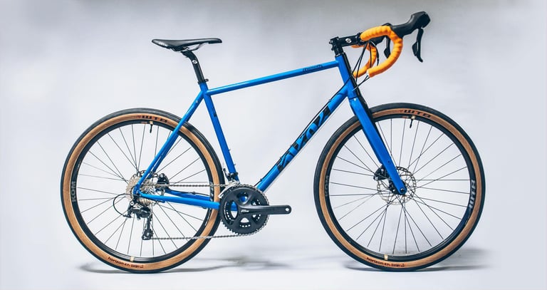 Cotic Escapade in blue with orange bar tape and tan-wall WTB Horizon tyres, side view against a plain studio backdrop.