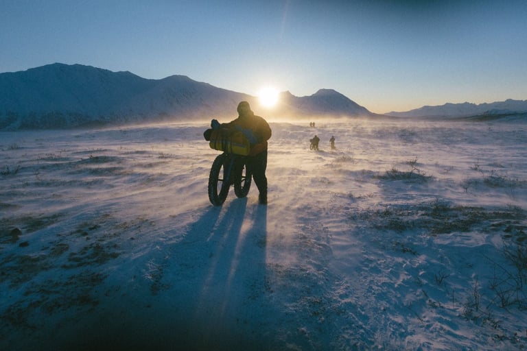 Riders strung out across open snow beneath a low sun, the long way to Nome in the Iditarod Trail Invitational.