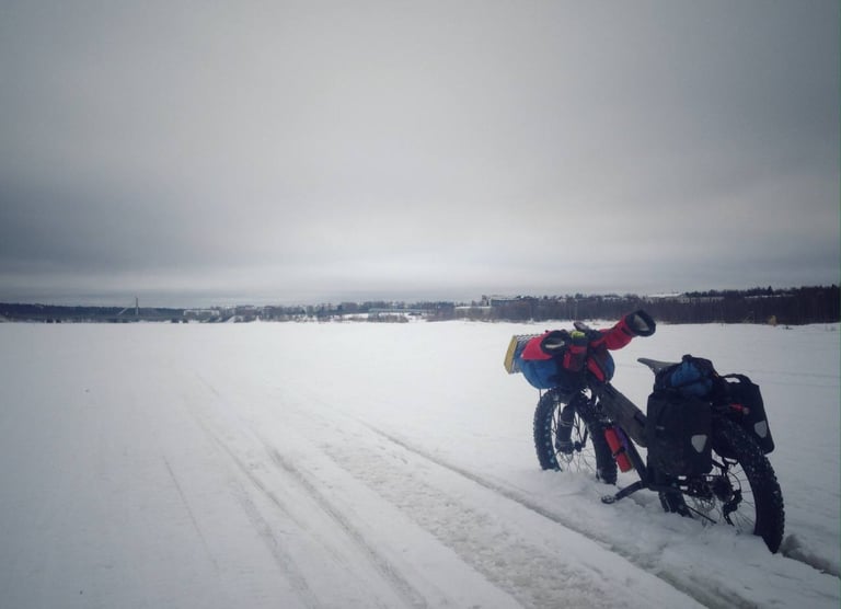 Salsa Mukluk fat bike loaded with panniers and a handlebar harness, parked on snow-covered ice near Rovaniemi.