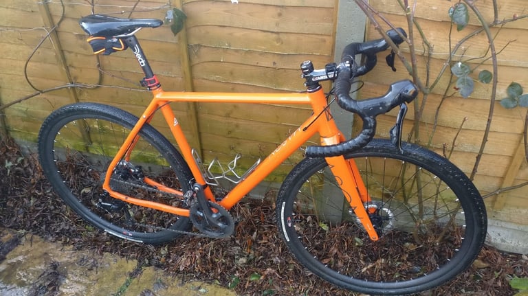 Orange gravel bike with drop bars and disc brakes, clean after washing with Proper Cleaner, against a wooden fence.
