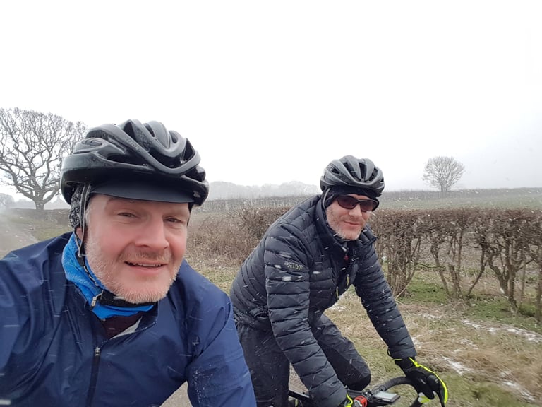Two riders in helmets and winter layers smile through snow flurries on the Cambridge Pork Pie Run.