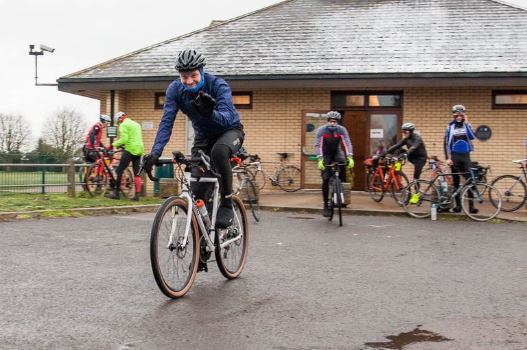 Riders set off from the start of the Cambridge Pork Pie Run, one waving at the camera, on a grey winter morning.