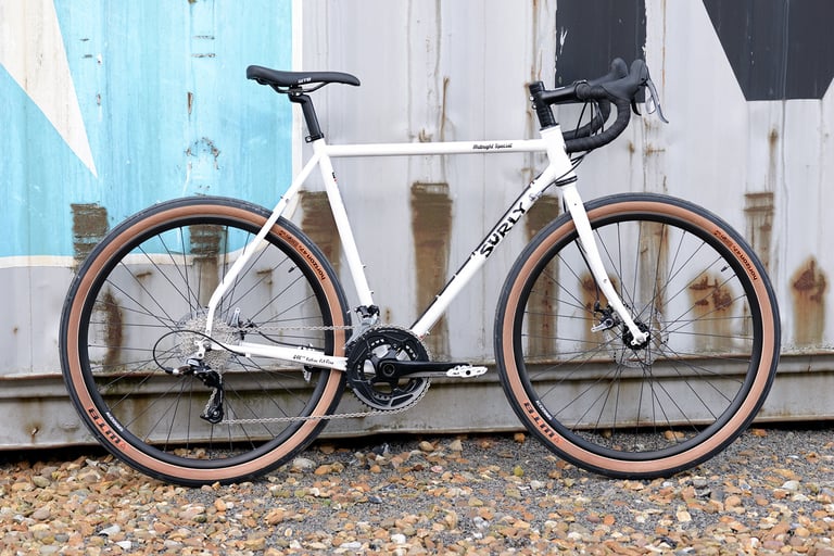 White Surly Midnight Special with tan-wall WTB Horizon tyres against a rusty blue and white container.