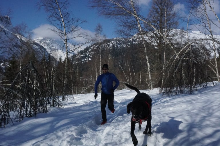 Runner in the Gore Primaloft jacket and trousers on a snowy mountain track, with a black dog bounding ahead.