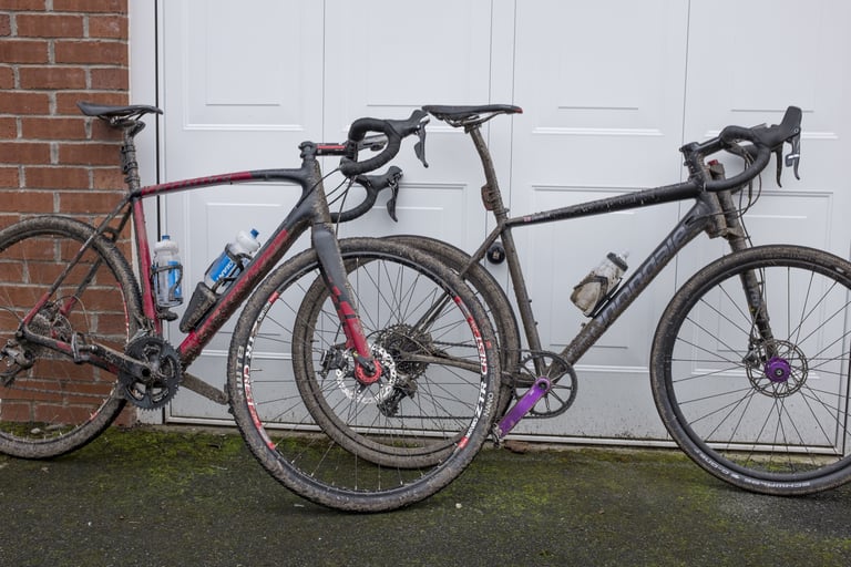 Muddy Cannondale Slate leaning against a white garage door next to a red and black gravel bike.