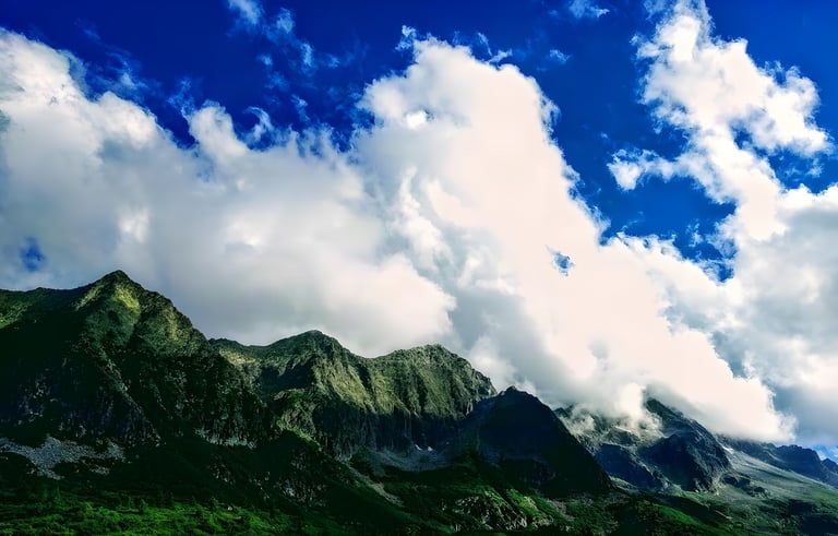 Green Alpine peaks below towering white cloud and blue sky on the Transalp route.