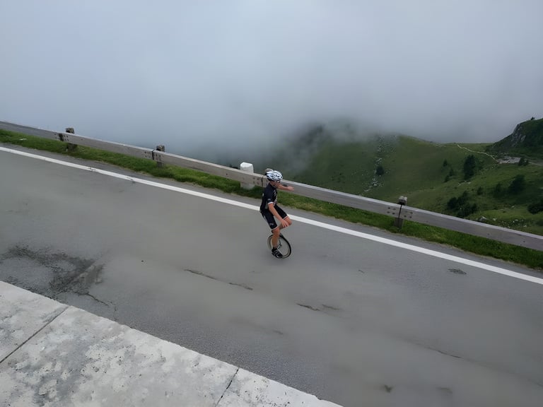 Unicyclist in a white helmet rides along a misty road near the top of Monte Grappa, the Transalp finish.