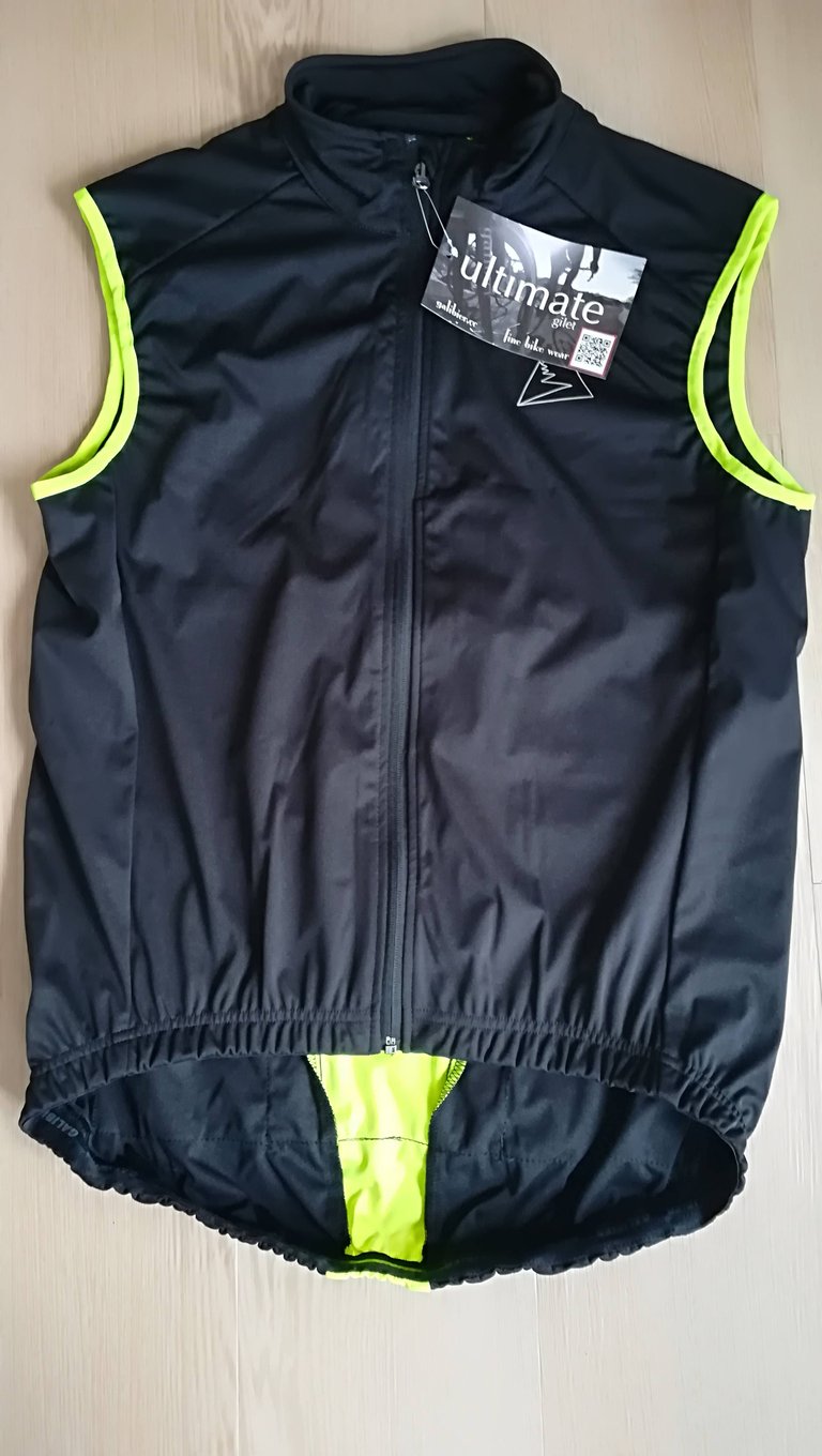 Galibier Ultimate Foul Weather Gilet laid flat, front view, in black with yellow piping and the swing tag attached.