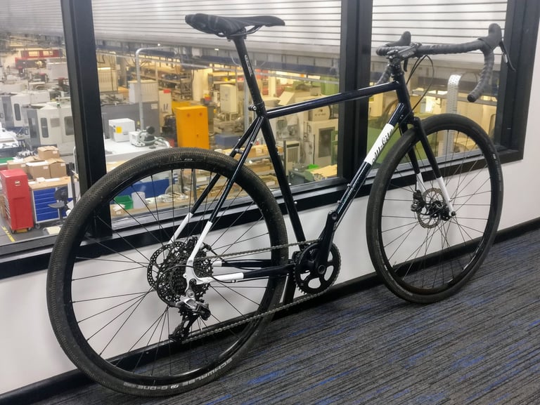 All-City Macho Man with SRAM Rival 1x drivetrain propped against an office window above a factory floor.