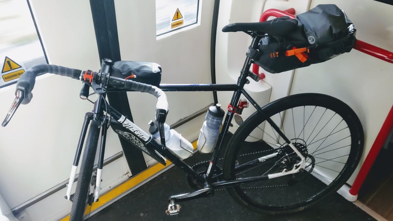 All-City Macho Man with an Ortlieb seat pack and bar bag stands inside a train carriage heading back to Cambridge.