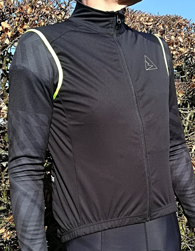 Front of the Galibier Ultimate gilet worn over a black long-sleeve jersey, full-length zip done up, in front of a hedge.