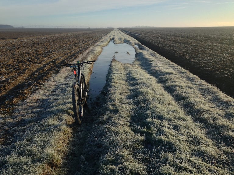 Mountain bike beside a puddle on a frosty grass track between ploughed fields on a winter commute.