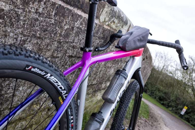 Close view of the Salsa Cutthroat's purple and pink fade frame, top-tube bag, bottle cages and Vittoria Mezcal tyre.