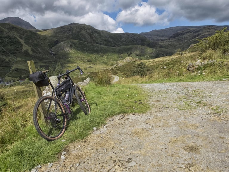 Cannondale Slate with bags leaning on a post beside a gravel track below the mountains of Snowdonia.