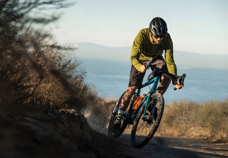 Rider in an olive top corners on a teal Salsa Journeyman along a dirt track with open water behind.