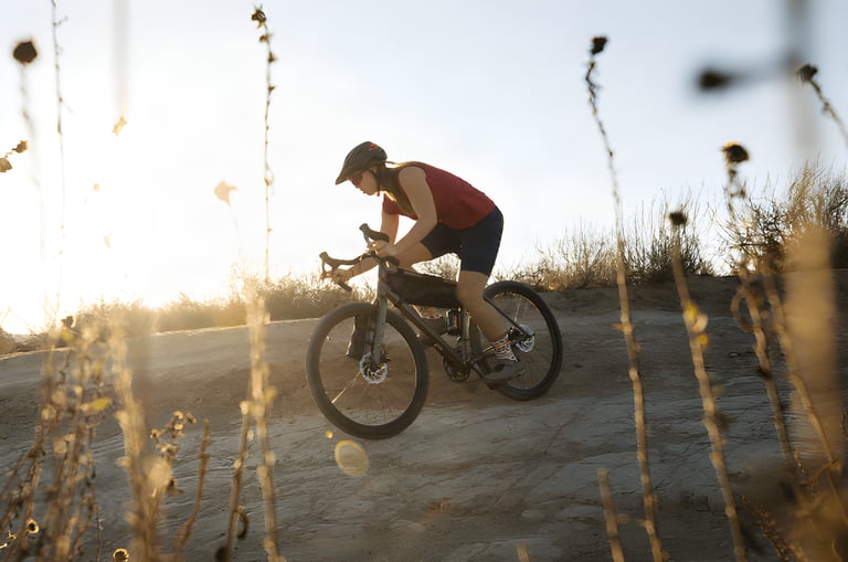 Rider in a red top leans into a gravel descent on a Salsa Journeyman with a top tube bag, backlit by low sun.
