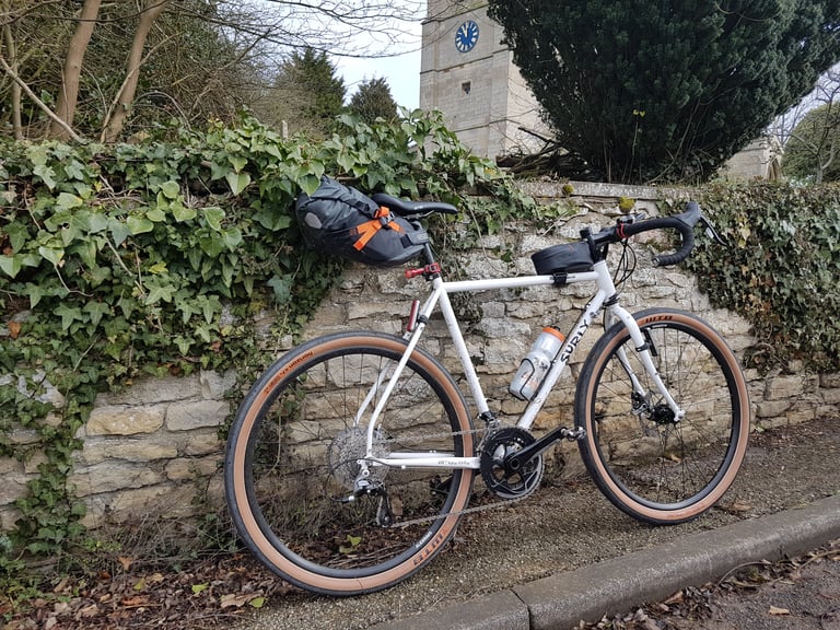 Surly Midnight Special with saddlebag and bottle leaning on an ivy-covered wall by a church.
