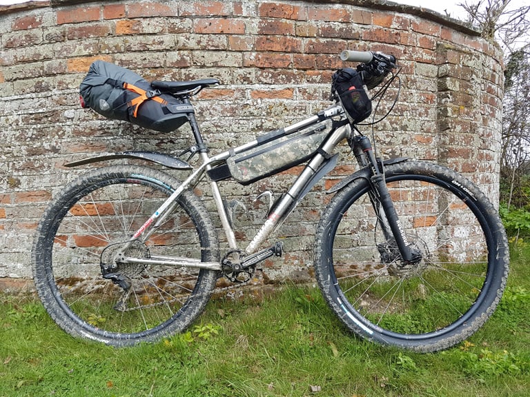 Ortlieb Seat-Pack fitted to a mud-splashed mountain bike with a frame bag and mudguards, leaning on a brick wall.