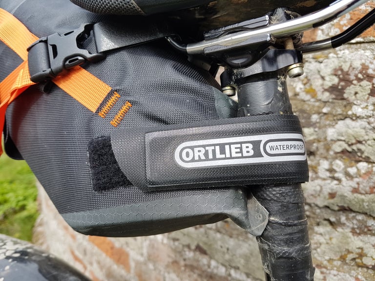 Close-up of the Ortlieb seat pack's reinforced taper and orange buckle strap where it wraps the seatpost.