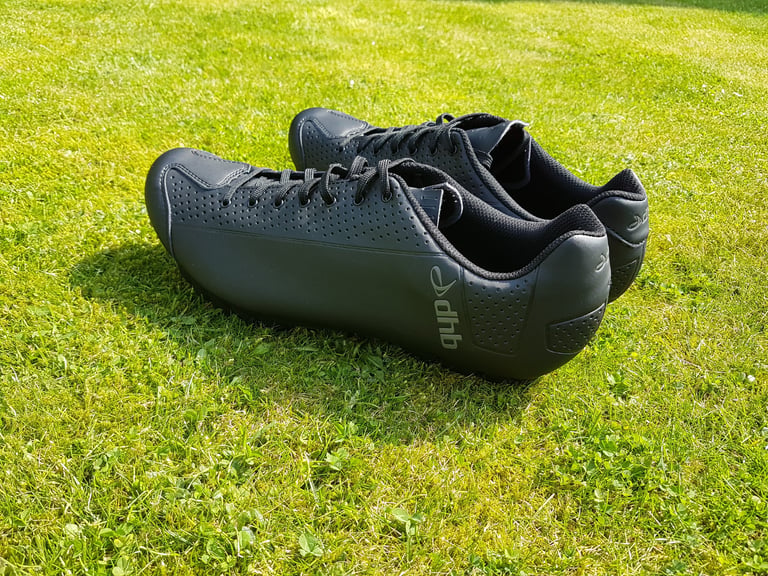 Black dhb Dorica lace-up cycling shoes on grass, seen from the heel and side.