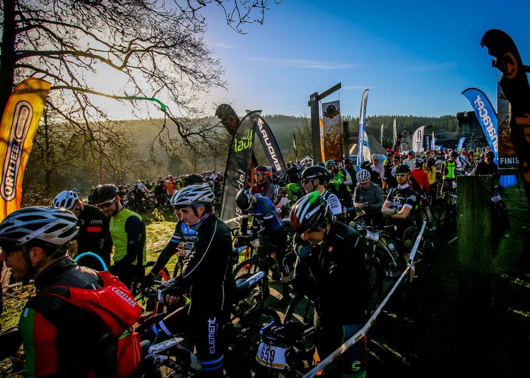 Crowded Dirty Reiver start line at Kielder, riders in helmets and winter kit waiting in low sun beside flags and tape.