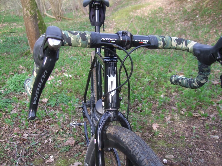 Fearless Vulture's camo-wrapped Ritchey handlebar, stem and head tube seen from the front on a leafy woodland trail.