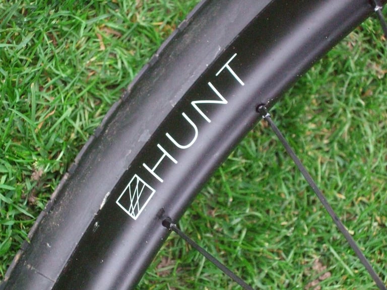 Close-up of the Hunt logo on a 30 Carbon Gravel rim with a tyre fitted, on grass.