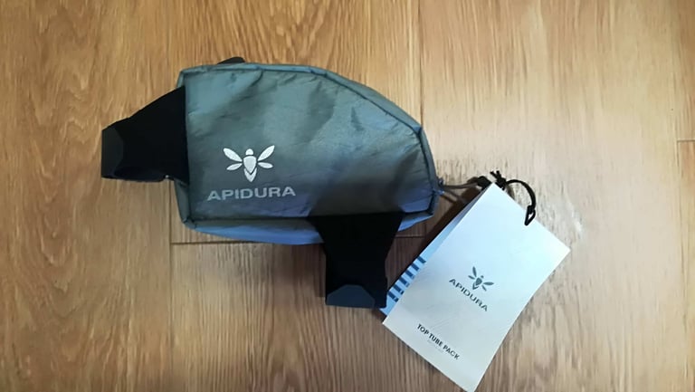 Apidura Backcountry Top Tube Bag with velcro straps and product tag, laid on a wooden floor.