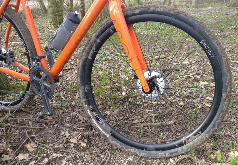 Mud-caked Hunt 30 Carbon Gravel front wheel on the orange Mason Bokeh after a ride on woodland trails.
