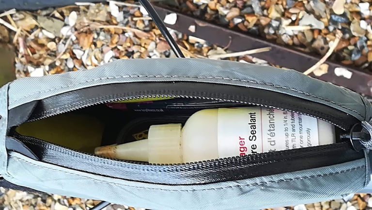 Open Apidura top tube bag holding a bottle of tubeless sealant, with a yellow lining.